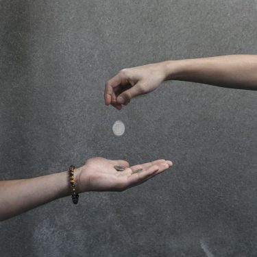 Hand lässt Münzen in andere Hand fallen. Geldspende. DE