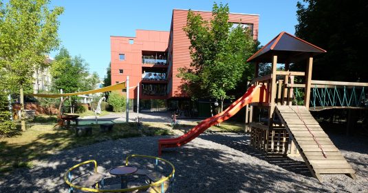 Kinderhaus Holee: Weitläufiger Aussenbereich mit Spielplatz. Im Hintergrund sind man das Wohngebäude.