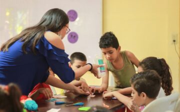 Eine Frau überreicht ein Glas Wasser an einen Jungen aus einer Kindergruppe.